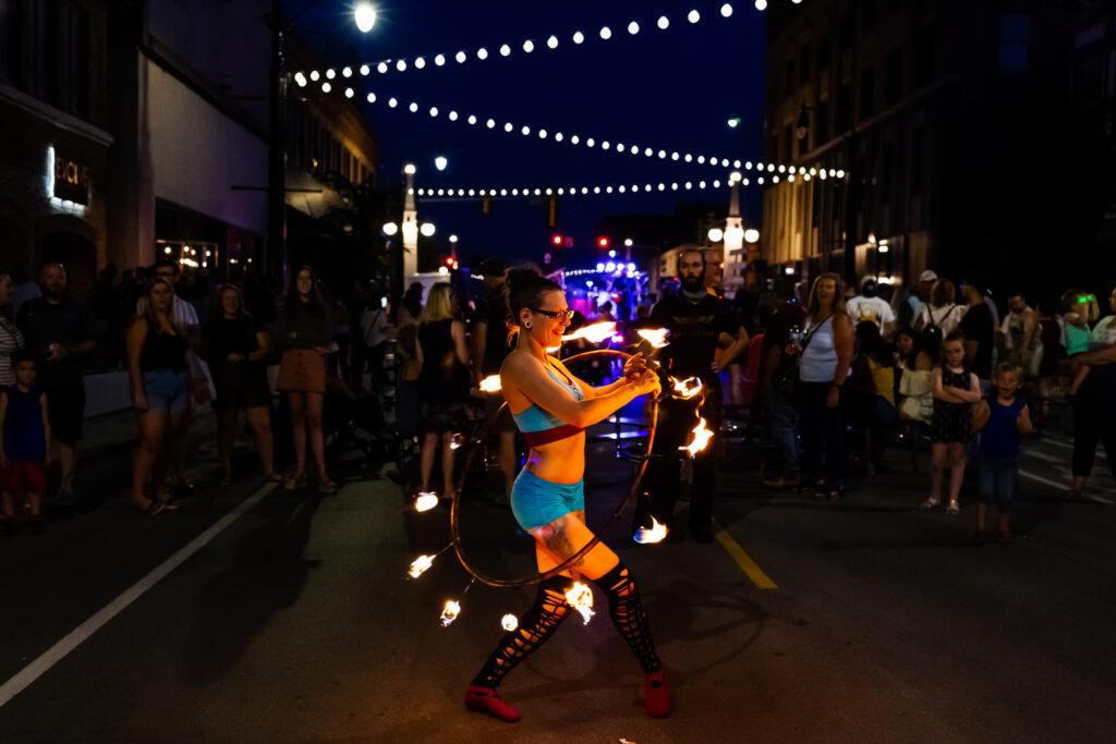 women twirling fire on a hula hoop in the middle of a road with people watching behind her